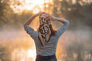 Foulard léopard porté sur la tête de dos avec une lumière du matin à la campagne, la femme porte une marinière et un jeans et son foulard imprimé leopard 